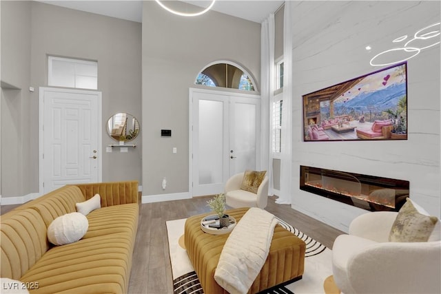 living room featuring a glass covered fireplace, a towering ceiling, baseboards, and wood finished floors