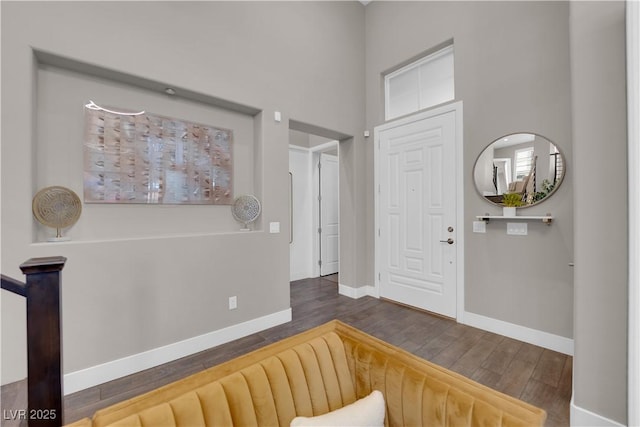 entrance foyer with dark wood-style floors, a towering ceiling, and baseboards