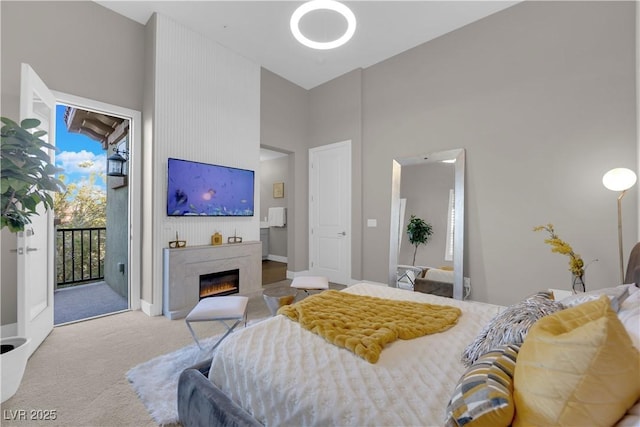 bedroom featuring access to outside, a high ceiling, light colored carpet, and a glass covered fireplace