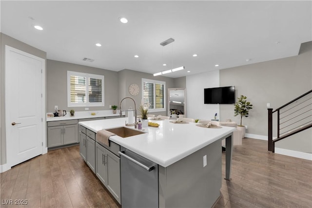 kitchen with hanging light fixtures, a kitchen island with sink, light countertops, and stainless steel dishwasher