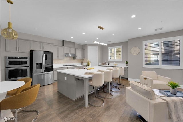 kitchen with a center island with sink, appliances with stainless steel finishes, a breakfast bar, hanging light fixtures, and light countertops