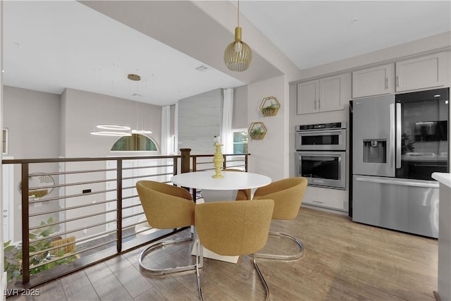 kitchen with stainless steel appliances, visible vents, hanging light fixtures, light wood-style flooring, and gray cabinetry