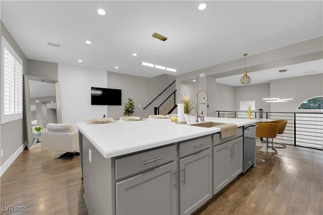 kitchen featuring pendant lighting, light countertops, gray cabinetry, open floor plan, and a kitchen island with sink