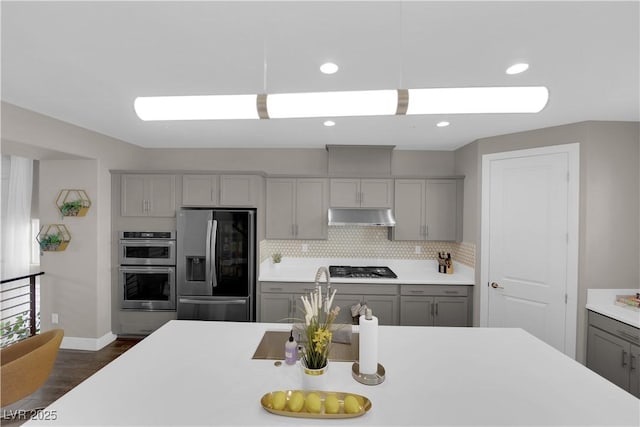 kitchen with gray cabinetry, stainless steel appliances, light countertops, and under cabinet range hood