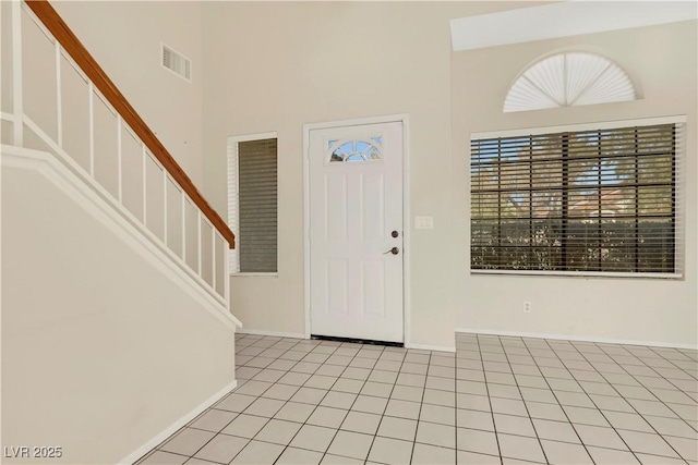 entrance foyer with light tile patterned floors, visible vents, a high ceiling, baseboards, and stairs