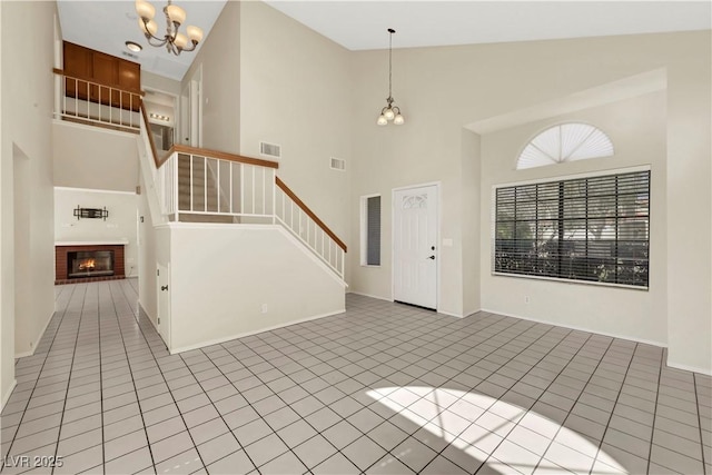 entryway featuring light tile patterned floors, visible vents, stairway, an inviting chandelier, and a brick fireplace