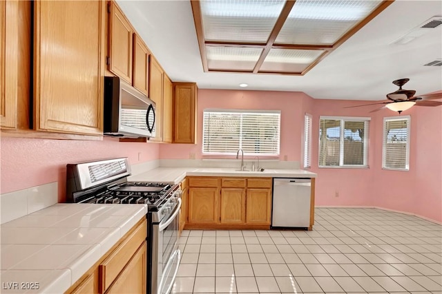 kitchen with stainless steel appliances, a wealth of natural light, a sink, and tile counters