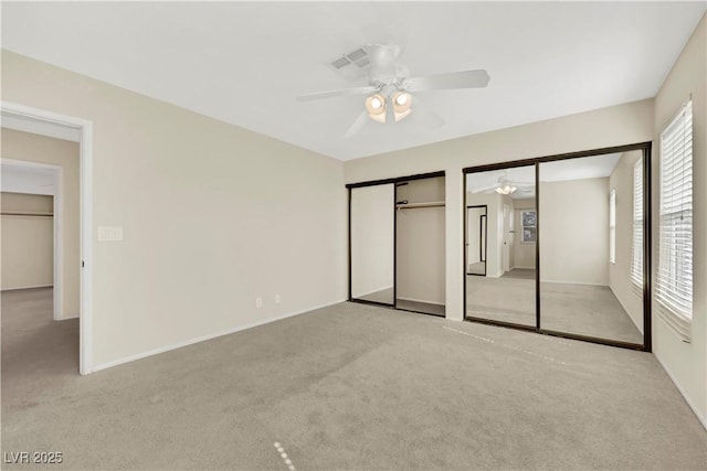 unfurnished bedroom with light carpet, ceiling fan, two closets, and baseboards