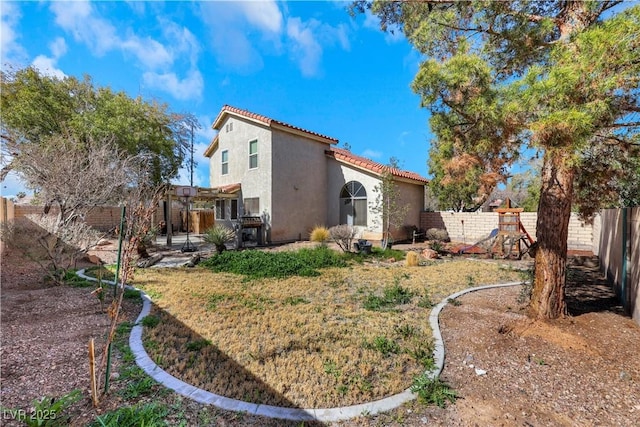 back of house with a playground, stucco siding, a pergola, a fenced backyard, and a tiled roof