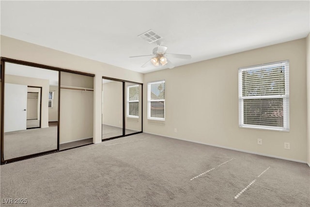 unfurnished bedroom with multiple windows, visible vents, two closets, and light colored carpet