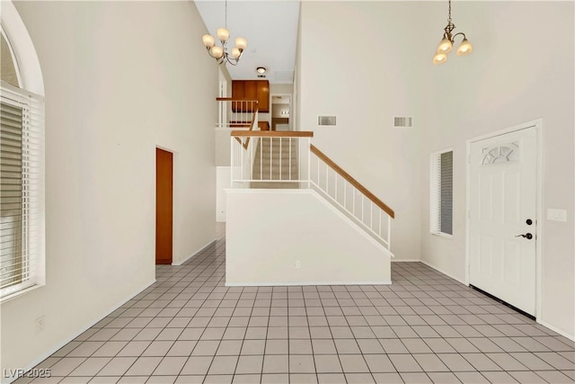 entryway with a towering ceiling, light tile patterned floors, visible vents, and a chandelier