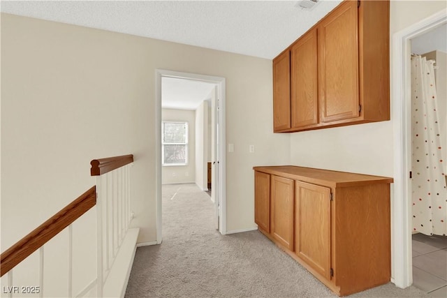 hallway with visible vents, light colored carpet, a textured ceiling, and an upstairs landing