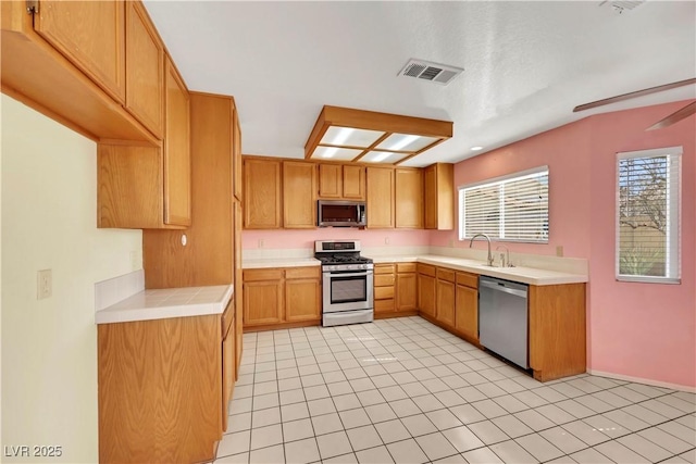 kitchen featuring visible vents, brown cabinetry, appliances with stainless steel finishes, light countertops, and a sink