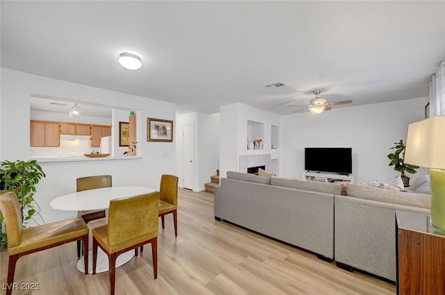 dining room with ceiling fan, a tiled fireplace, visible vents, and light wood-style floors