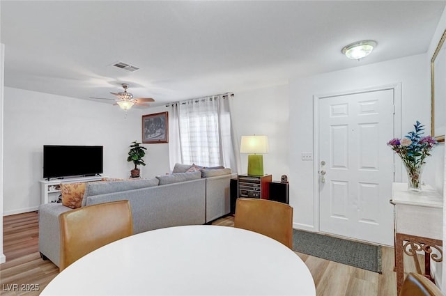 living area featuring baseboards, visible vents, ceiling fan, and light wood finished floors