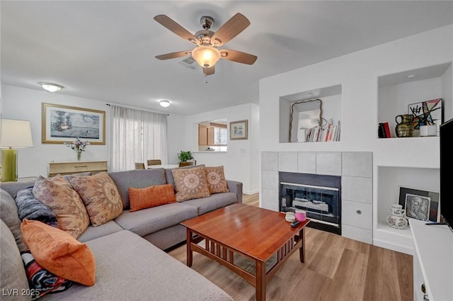 living room featuring a fireplace, light wood finished floors, visible vents, a ceiling fan, and baseboards