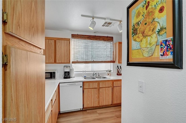 kitchen with a sink, light wood finished floors, light countertops, and dishwasher