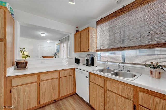 kitchen featuring light countertops, white dishwasher, a sink, and light wood-style flooring