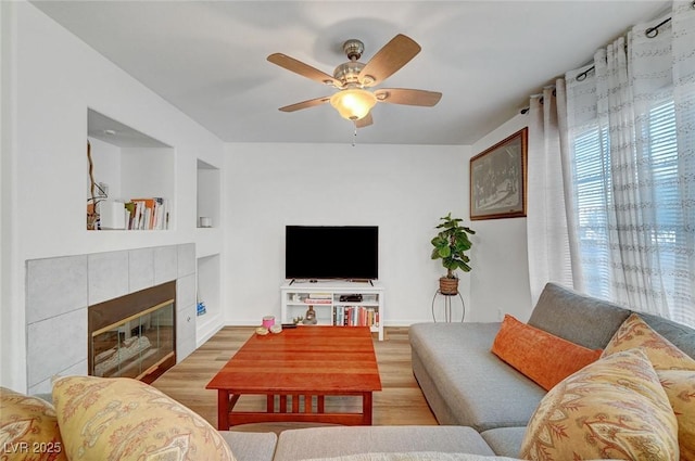 living area featuring a tile fireplace, ceiling fan, baseboards, and wood finished floors