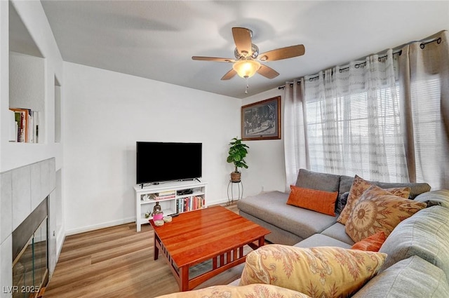 living area with ceiling fan, baseboards, a tiled fireplace, and wood finished floors