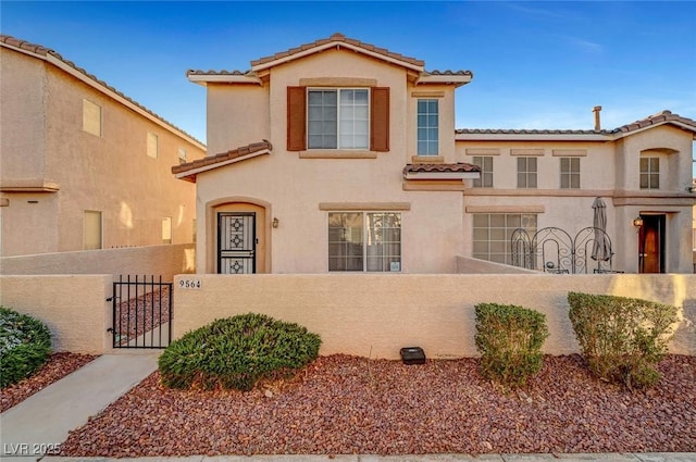 mediterranean / spanish home featuring a tile roof, a fenced front yard, a gate, and stucco siding