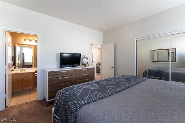 bedroom with light tile patterned floors, a closet, light colored carpet, ensuite bathroom, and a sink