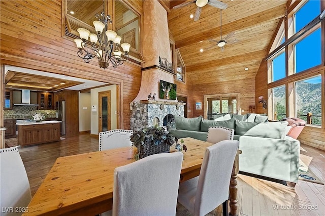 dining space featuring a fireplace, dark wood-type flooring, wood ceiling, wooden walls, and ceiling fan with notable chandelier