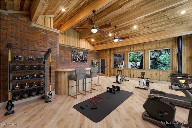 exercise room featuring lofted ceiling, wooden ceiling, wooden walls, light wood finished floors, and a wood stove