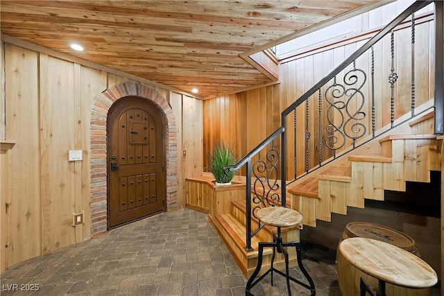 foyer featuring brick floor, wood walls, a skylight, wood ceiling, and stairway