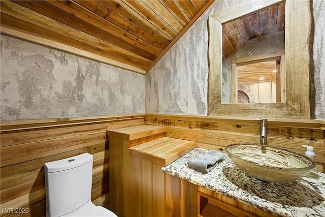 half bath with toilet, wooden ceiling, vaulted ceiling, and vanity