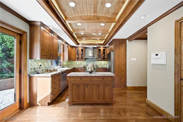 kitchen featuring a center island, brown cabinets, light countertops, glass insert cabinets, and wall chimney exhaust hood