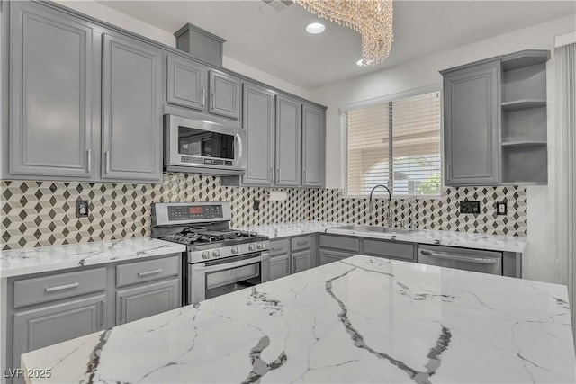 kitchen with light stone counters, stainless steel appliances, gray cabinetry, open shelves, and a sink