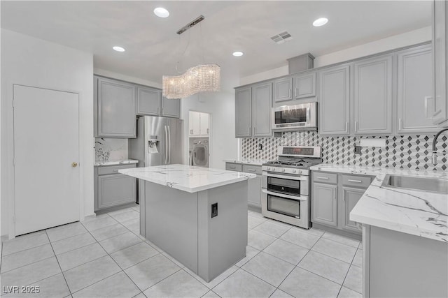 kitchen with stainless steel appliances, a sink, visible vents, a kitchen island, and decorative light fixtures