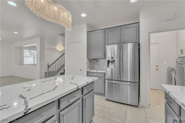 kitchen featuring light stone counters, decorative light fixtures, gray cabinets, backsplash, and stainless steel fridge with ice dispenser