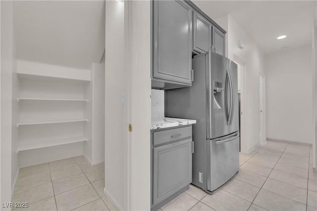 kitchen featuring light tile patterned flooring, gray cabinets, light stone countertops, and stainless steel fridge with ice dispenser