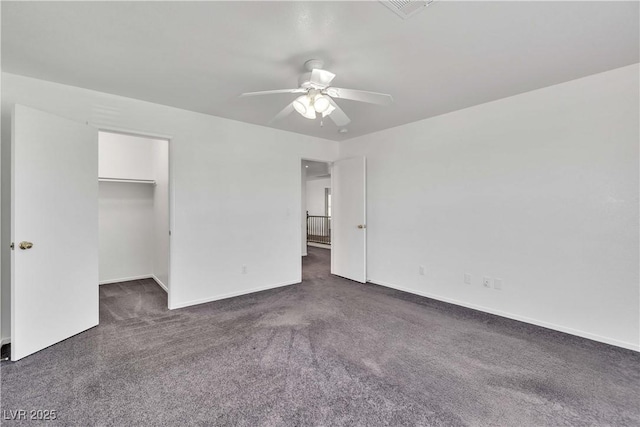 unfurnished bedroom featuring dark carpet, a spacious closet, baseboards, and ceiling fan