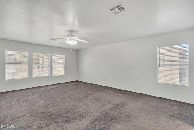 spare room featuring dark colored carpet, visible vents, and ceiling fan