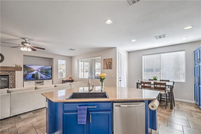 kitchen with blue cabinetry, stainless steel dishwasher, open floor plan, a kitchen island with sink, and a sink