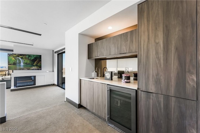 kitchen with light colored carpet, beverage cooler, a fireplace, a sink, and light countertops