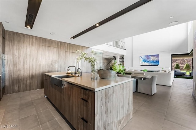 kitchen featuring a center island with sink, light countertops, wood walls, a sink, and modern cabinets