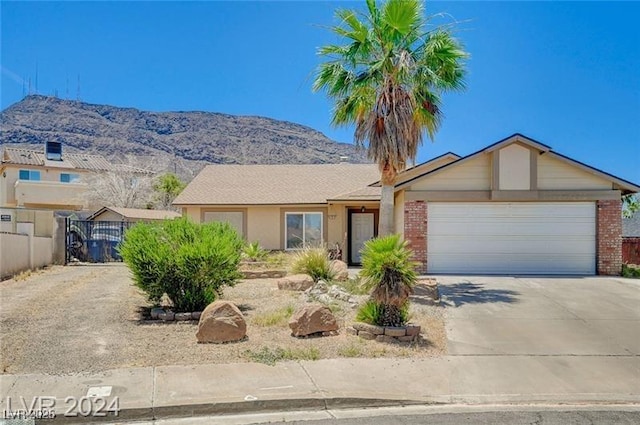 ranch-style house with brick siding, a mountain view, fence, a garage, and driveway