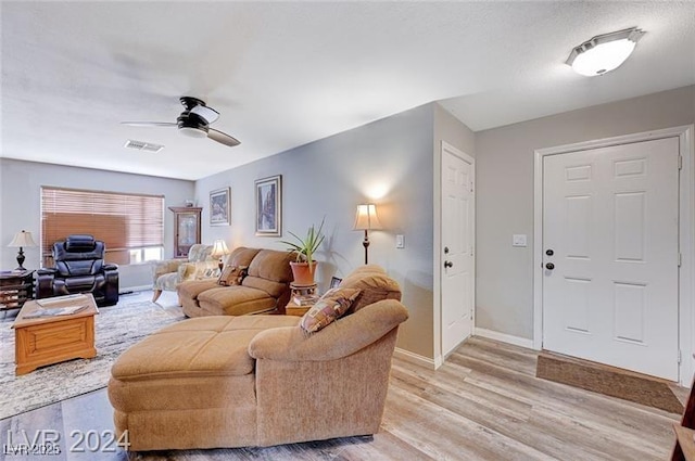 living room featuring light wood-type flooring, visible vents, ceiling fan, and baseboards