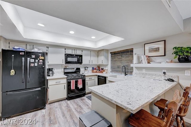 478 Potomac St, Henderson, NV 89015 - kitchen featuring a peninsula, a sink, black appliances, light wood finished floors, and a tray ceiling