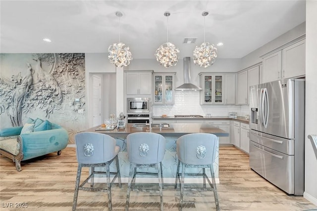 kitchen with visible vents, appliances with stainless steel finishes, wall chimney range hood, light wood-type flooring, and tasteful backsplash