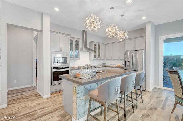 kitchen featuring wall chimney range hood, light wood-style flooring, appliances with stainless steel finishes, and a sink