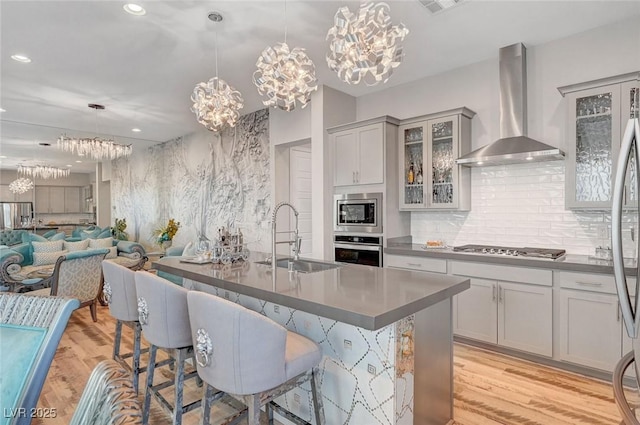 kitchen with wall chimney exhaust hood, light wood-style flooring, a breakfast bar area, stainless steel appliances, and a sink