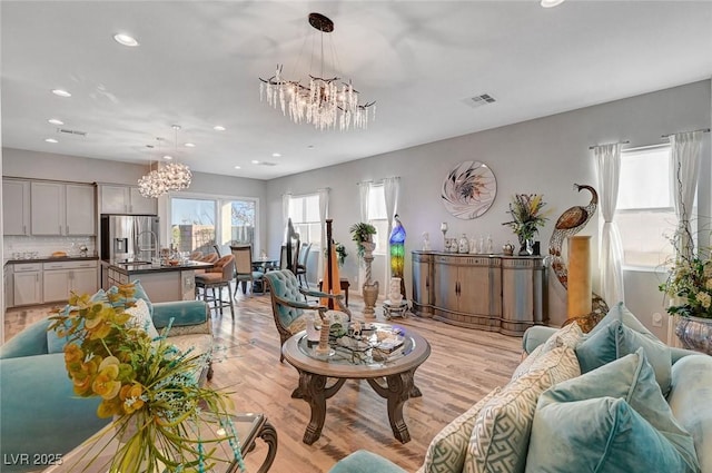 living area featuring plenty of natural light, a notable chandelier, and light wood-style flooring