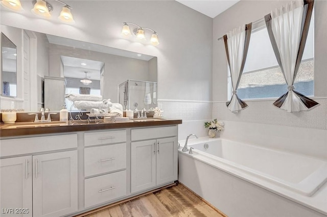 bathroom featuring double vanity, a stall shower, wood finished floors, a garden tub, and a sink