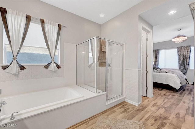 bathroom with ensuite bath, wood finished floors, an inviting chandelier, a shower stall, and a bath