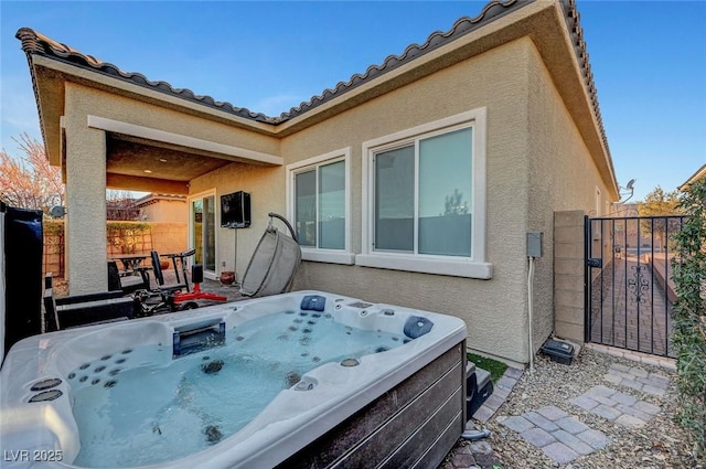 back of house featuring a hot tub, a gate, fence, and stucco siding